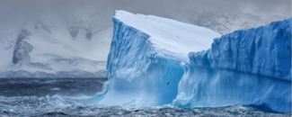 Massive iceberg floating in the Southern Ocean off Antarctica with snow-covered mountains in the background. Courtesy of GettyImages. Credit: Ray Hems.